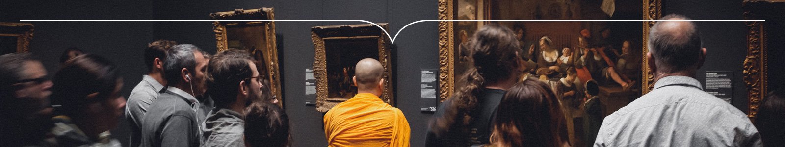 Kale monnik in oranje toga staat tussen toeristen voor een schilderij in een museum