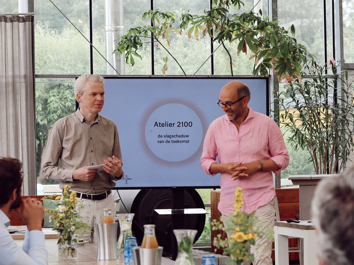 two middle ages men presenting in front of screen, setting is a glass green house