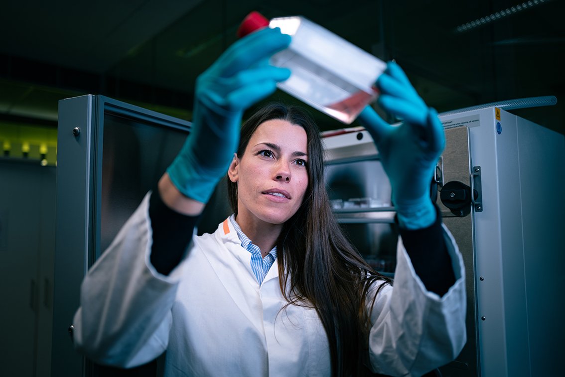 Een onderzoeker houdt een fles met rode vloeistof in het licht en kijkt ernaar.