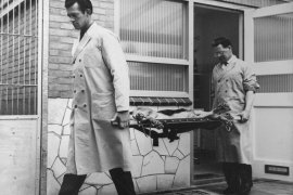 Black and white photo from the sixties. Two Veterinarians carrying a dog outside on a strecher.