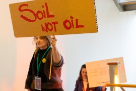 woman holding protest sign 'Soil not oil'