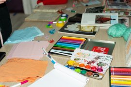 a table with pieces of fabric, paint, colouring pencils, coloured tape and markers