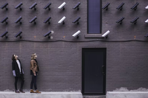 Two people looking at a wall full of security cameras