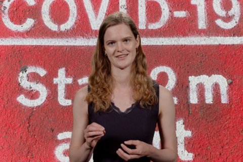 Veerle Dijkstra voor een rode achtergrond waarop in grote letters 'COVID-19' staat. Screenshot uit het filmpje waarin alle vier de genomineerden over hun scriptie vertellen.