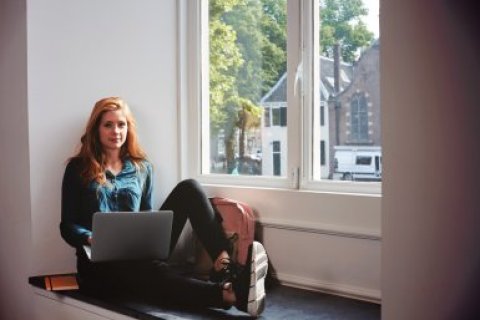 Student zittend in vensterbank met laptop (UB Binnenstad)
