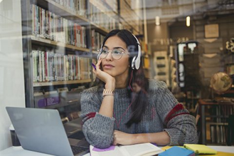 Vrouwelijke student zit in de bibliotheek en luistert een podcast met een koptelefoon op