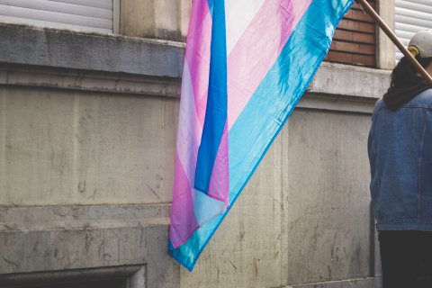 Tegen een gebouw hangt de transgender vlag, in de kleuren blauw, roze en wit.