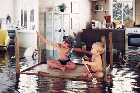 twee kinderen zitten op een tafel in een overstroomde woonkamer