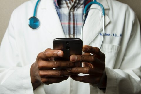 Arts met stethoscoop om de hals en smartphone in zijn handen