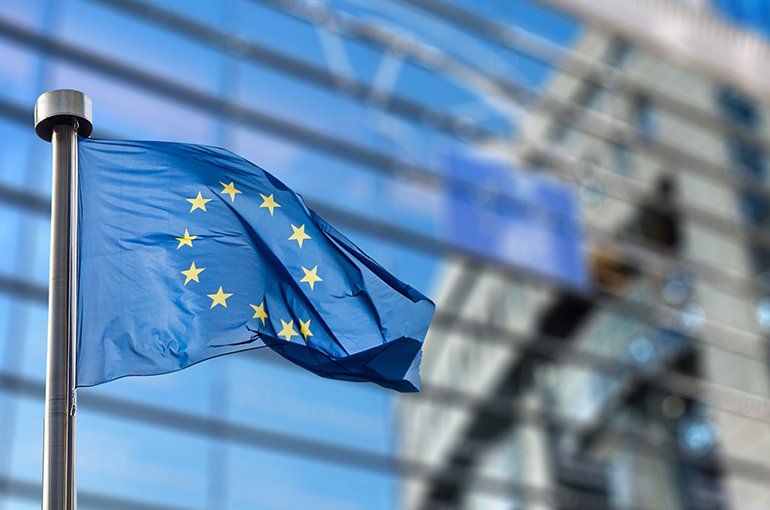 Vlag van de Europese Unie met op de achter grond het gebouw van de EU © iStockphoto.com/artJazz