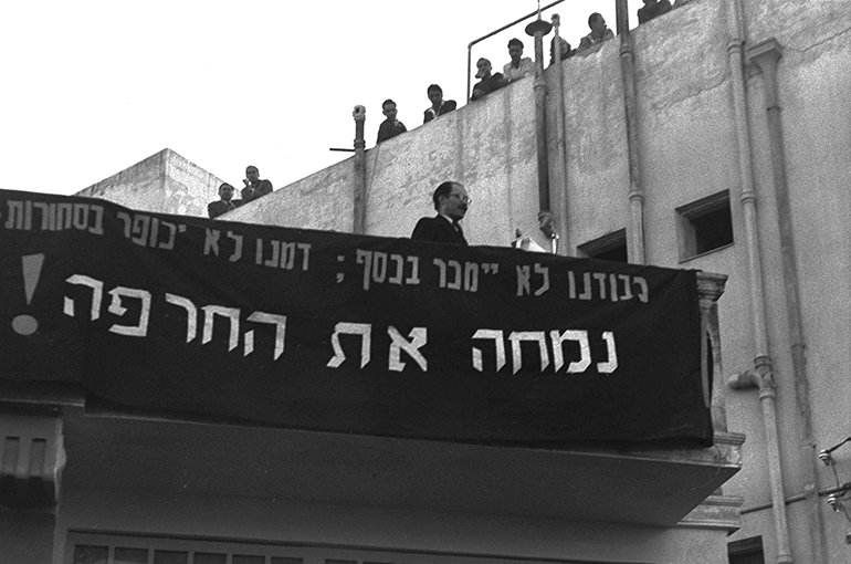 Menachem Begin protesteert tegen het Verdrag van Luxemburg (Wassenaar-akkoord). Op het spandoek staat: "Onze eer zal niet voor geld worden verkocht; Ons bloed zal niet worden vergoed met goederen. We zullen de schande tenietdoen!" Bron: Wikimedia/Hans Pinn