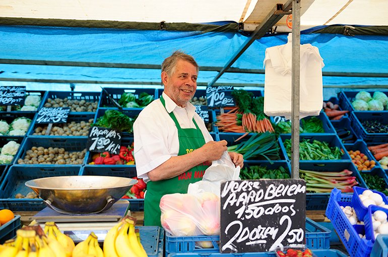 Een marktkoopman staat in zijn groentekraam © iStockphoto.com/VLIET