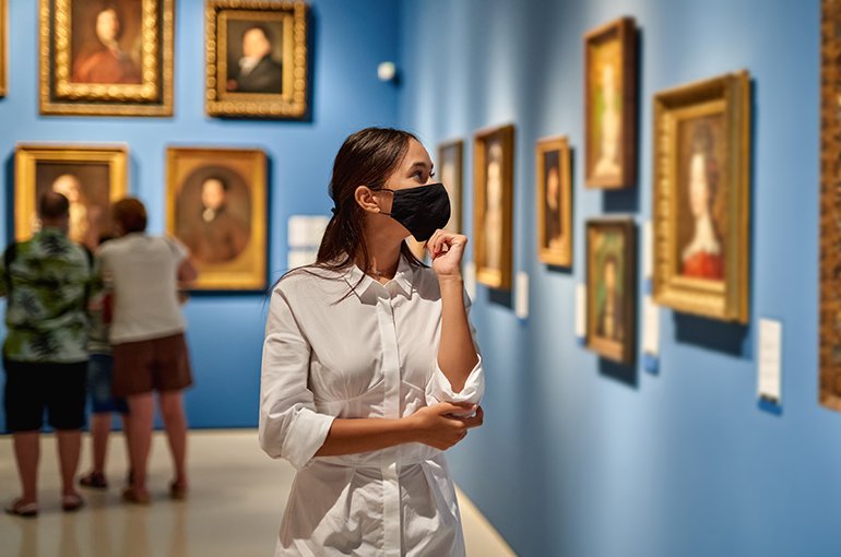 Een vrouw loopt in een museum met mondkapje op © iStockphoto.com/jenoche