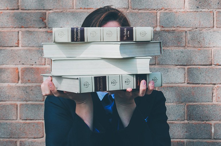 Een onderzoeker houdt boeken voor haar gezicht. Foto: Siora Photography, via Unsplash