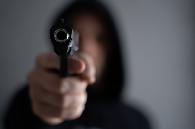 Een onscherpe persoon met een hoodie richt een pistool © iStockphoto.com/Viktoria Korobova