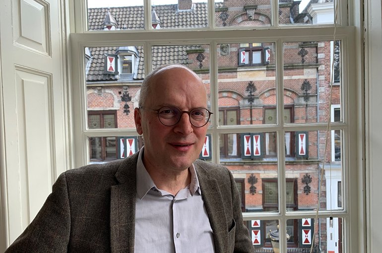portretfoto Marcel Verweij. Half-totaal, kale witte man met bril voor raam in Ethiek Instituut