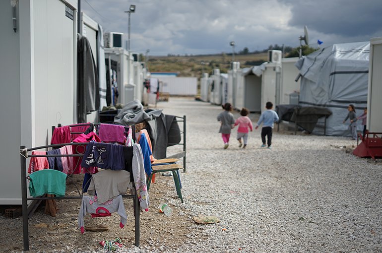 Een vluchtelingenkamp, met drie kinderen gezien op de rug. Foto: Julie Ricard, via Unsplash