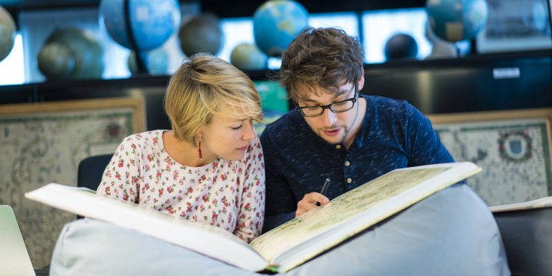 Onderzoekers bestuderen een atlas in de kaartenzaal van de Universiteitsbibliotheek Utrecht