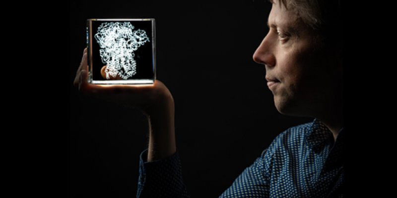 Onderzoeker Berend Jan Bosch kijkt in een model van een coronavirus dat in een doorzichtige kubus zit